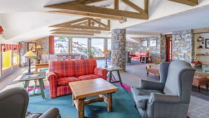 A spacious living area with a wooden ceiling, stone walls, a red plaid sofa, a grey armchair, and a wooden coffee table. - Beautiful apartment for 6 guests with pool, WIFI, TV, terrace and pets allowed (La Plagne)