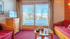 A cozy room with a wooden bed, a small table with breakfast items, a TV, and a window with a snowy view. - Beautiful apartment for 6 guests with pool, WIFI, TV, terrace and pets allowed (La Plagne)