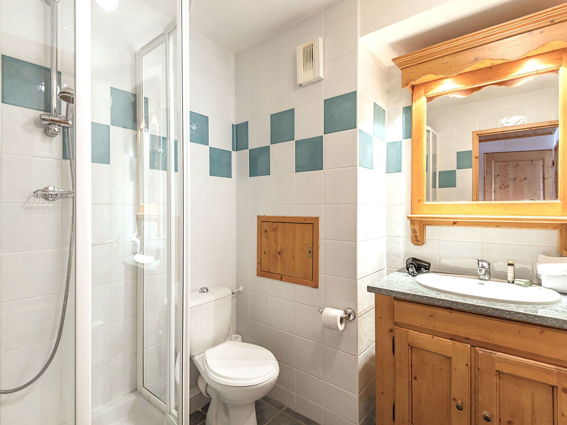 Une salle de bain avec une douche à parois de verre, des toilettes, un meuble en bois et un lavabo avec un miroir au-dessus.