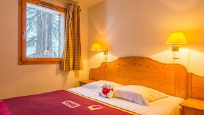 Ett hotellrum med en sänggavel i trä, två sänglampor, ett fönster med gardiner och en säng med ett rött överkast.