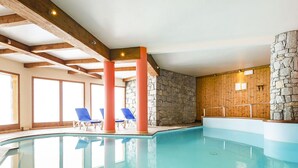 En inomhuspool med kristallklart blått vatten, träbjälkar, stenmurar och blå solstolar.