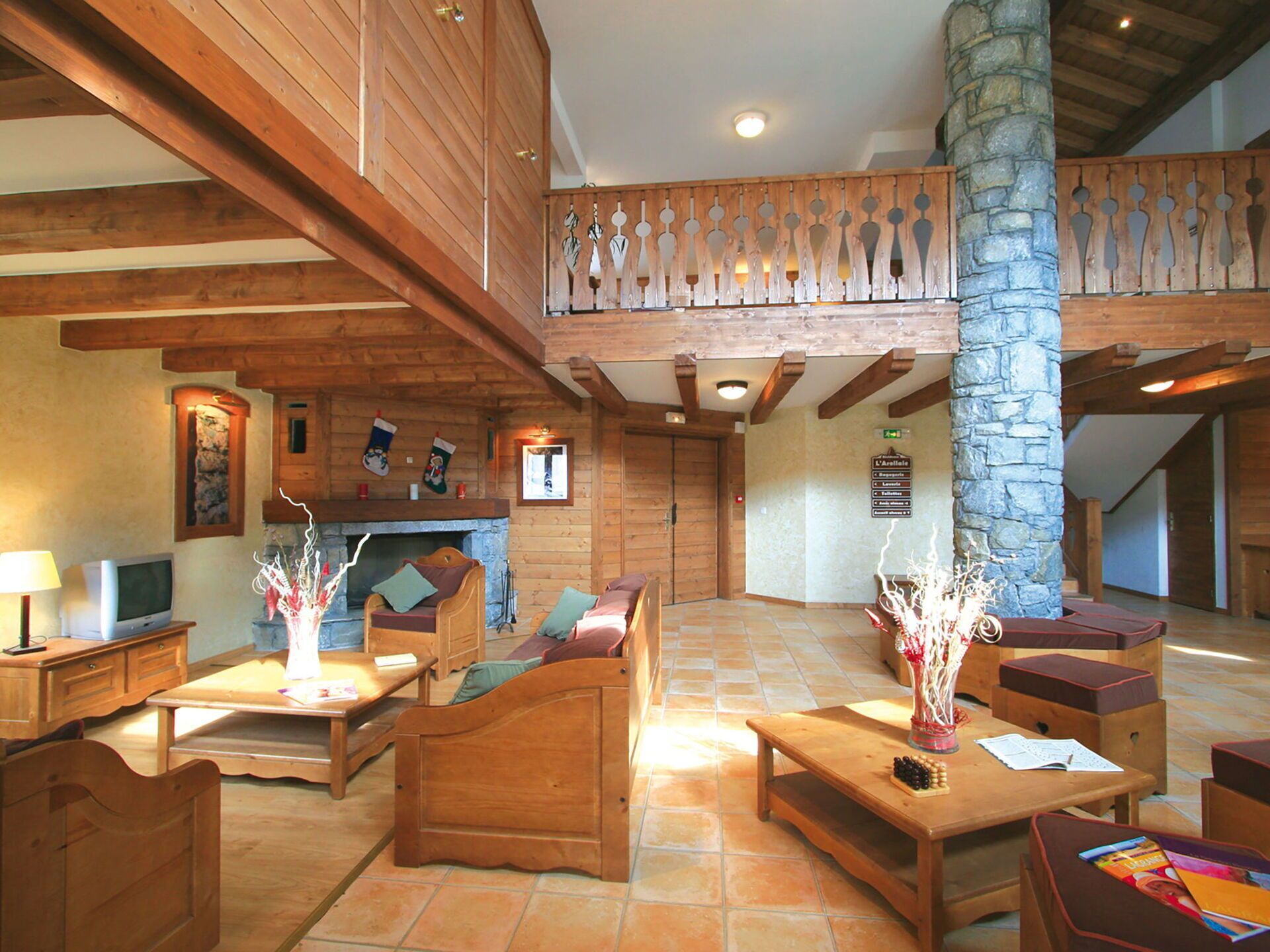 A wooden-floored lobby with a fireplace, seating area, and a stone pillar.