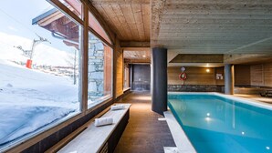 Ein Innenpool mit Steinwänden und Holzbalken, Bänke mit Handtüchern und Blick auf eine verschneite Landschaft.
