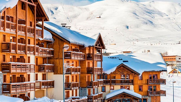 Ein Chalet-Hotel aus Holz mit mehreren Balkonen und einem Skiabhang im Hintergrund.
