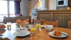 En frukostuppdukning med croissanter, kaffe och apelsinjuice på ett träbord.