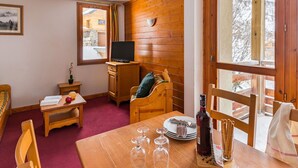 Um quarto aconchegante com paredes de madeira, uma mesa de jantar posta com taças de vinho, uma garrafa e um cesto de palitos de pão.