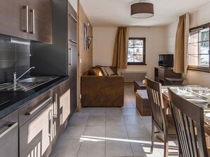 Una cocina moderna con encimera negra, electrodomésticos de acero inoxidable y un comedor con mesa y sillas de madera.