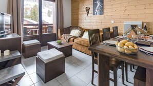 A cozy living room with a wooden wall, a sofa, a coffee table, a TV, and a dining area with a table set for two. - Lovely apartment for 6 people with WIFI, pool, TV, terrace and pets allowed (Les Gets)