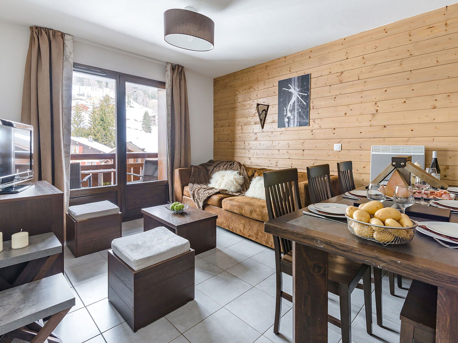 A cozy living room with a wooden wall, a sofa, a coffee table, a TV, and a dining area with a table set for two.