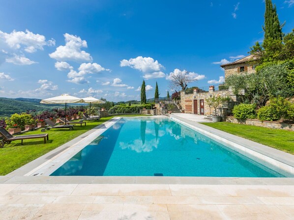 Relax by the rectangular pool surrounded by lush greenery and a traditional stone building.