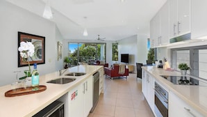 A modern kitchen with a central island, built-in appliances, and a dining area with a red sofa. - Top 1 Sunshine Beach Family Retreat (Sunshine Beach)