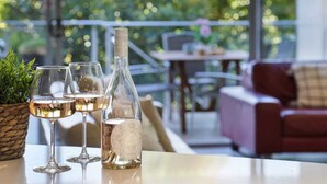 A table with two wine glasses and a bottle of wine, a potted plant, and a red couch in the background. - Top 1 Sunshine Beach Family Retreat (Sunshine Beach)