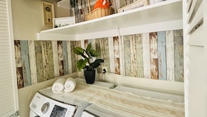 A laundry area with a washing machine and dryer, shelves with baskets and plants, and a wall with a rustic wooden panel design. - Frenzy for the old w/heatedpool in a safe and quite neighborhood! (Tampa)