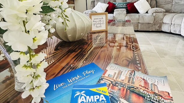 A living room with a sofa, a vase with white flowers, a framed quote, and brochures on the floor. - Frenzy for the old w/heatedpool in a safe and quite neighborhood! (Tampa)