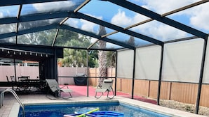 An indoor swimming pool with a pink inflatable ring, lounge chairs, and a covered patio area. - Frenzy for the old w/heatedpool in a safe and quite neighborhood! (Tampa)