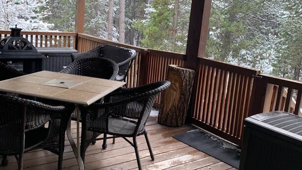 A covered outdoor deck with a wooden table and chairs, a red lantern, and a view of snow-covered trees. - Great family getaway with large entertaining deck. (Crescent Lake)