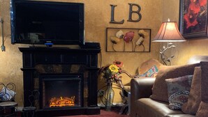 A living room with a fireplace, a sofa, a TV mounted above the fireplace, and a wall with the letters "LB". - Great family getaway with large entertaining deck. (Crescent Lake)