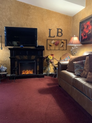 A living room with a fireplace, a sofa, a TV mounted above the fireplace, and a wall with the letters "LB". - Great family getaway with large entertaining deck. (Crescent Lake)