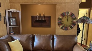A brown leather sofa with a small wooden table, a decorative wall clock, and a framed picture on a shelf. - Great family getaway with large entertaining deck. (Crescent Lake)