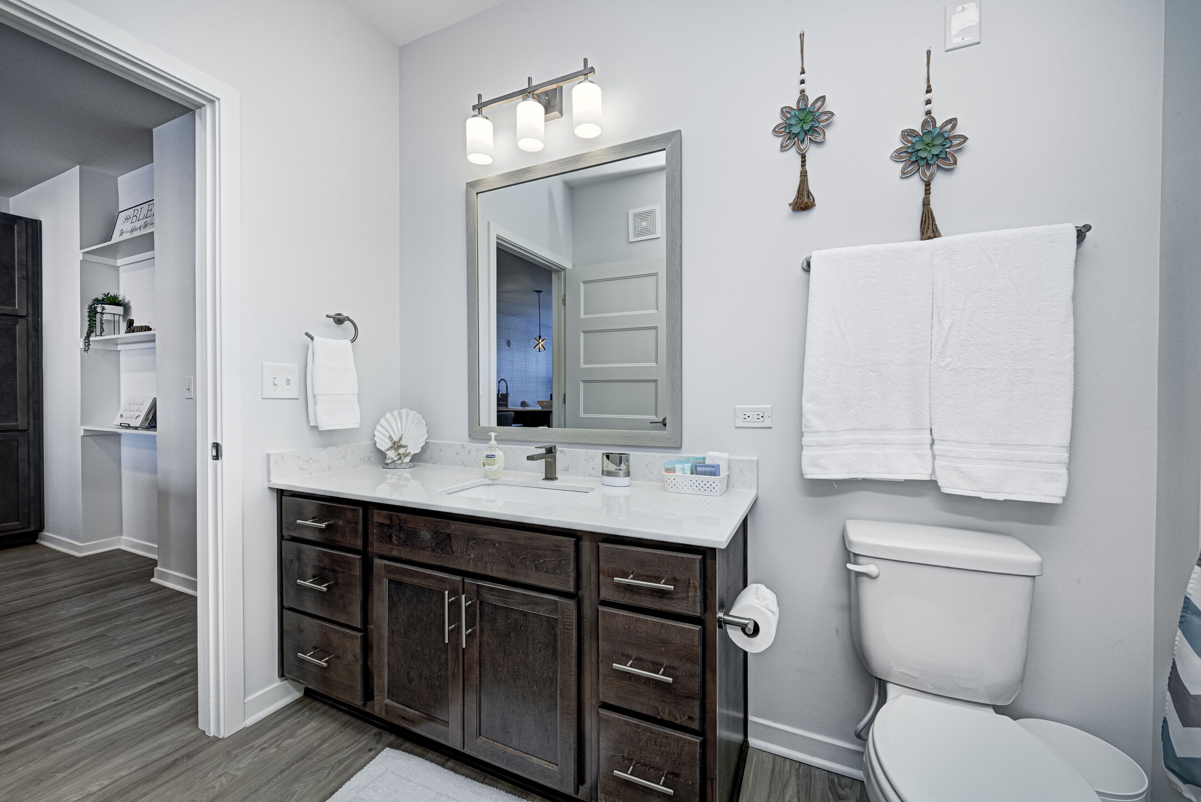 Une salle de bain moderne avec un meuble-lavabo blanc, des armoires en bois foncé, un grand miroir et des toilettes.