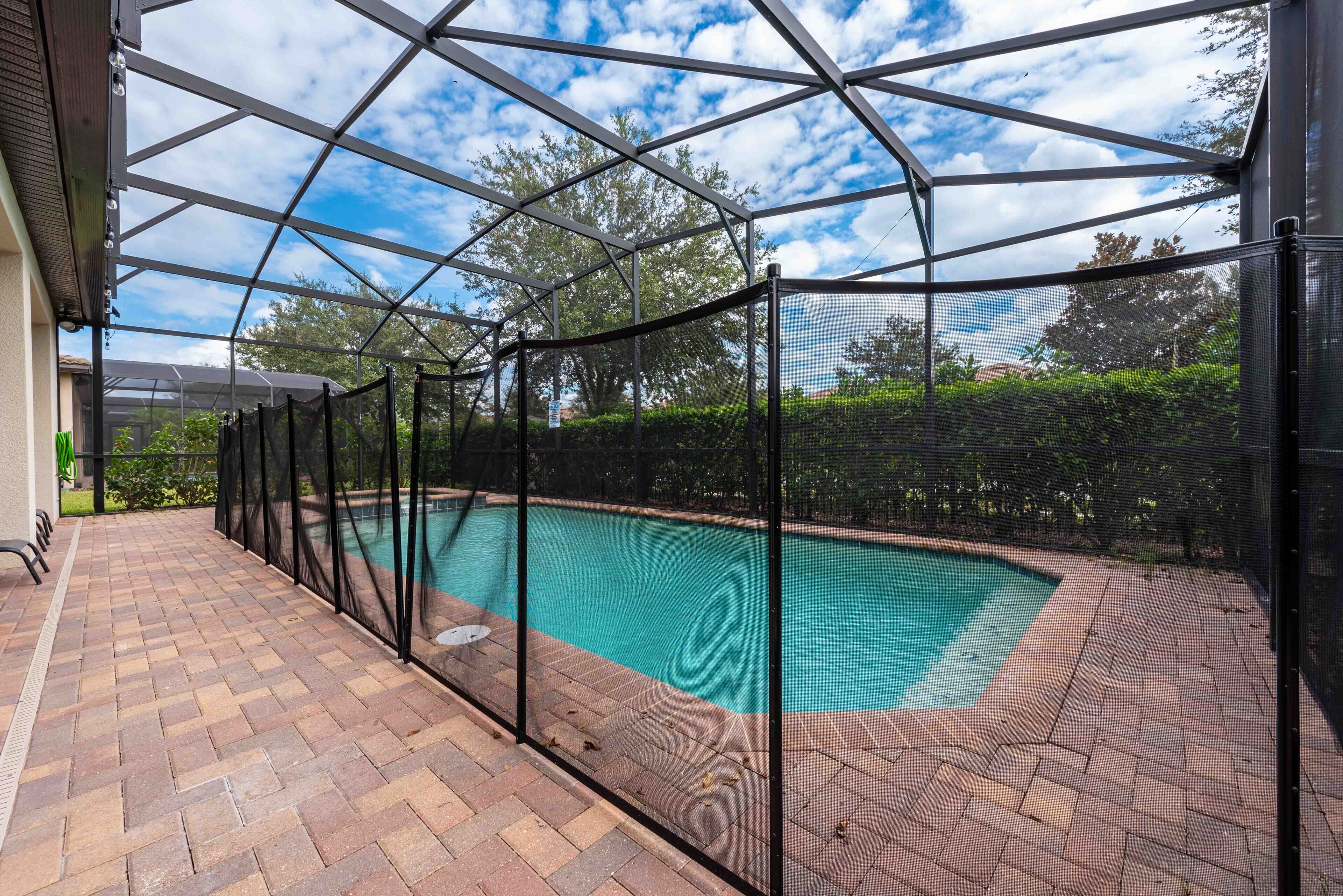 A covered swimming pool with a brick patio and a metal roof structure.