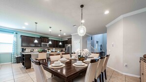 A modern kitchen with dark cabinets, a central island, and a dining area with a wooden table and chairs. - Huge Amazing Arcade Pool Home (Kissimmee)