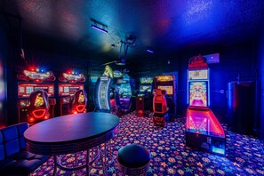 A room with arcade games, a round table, and a patterned carpet.