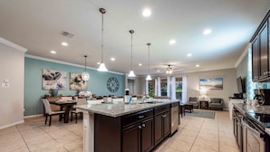 A spacious kitchen with dark cabinetry, a central island, pendant lighting, and a dining area with a table and chairs. - Huge Amazing Arcade Pool Home (Kissimmee)
