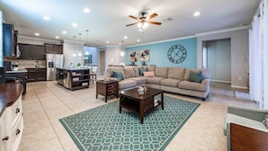 A spacious living area with a kitchen, a ceiling fan, and a large clock on the wall. - Huge Amazing Arcade Pool Home (Kissimmee)