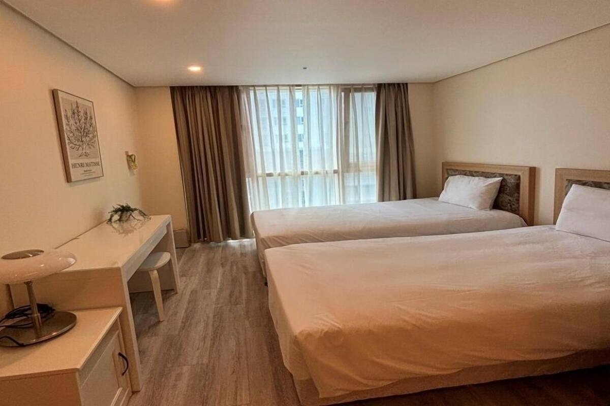 Habitación de hotel con dos camas, un escritorio y una ventana con cortinas.
