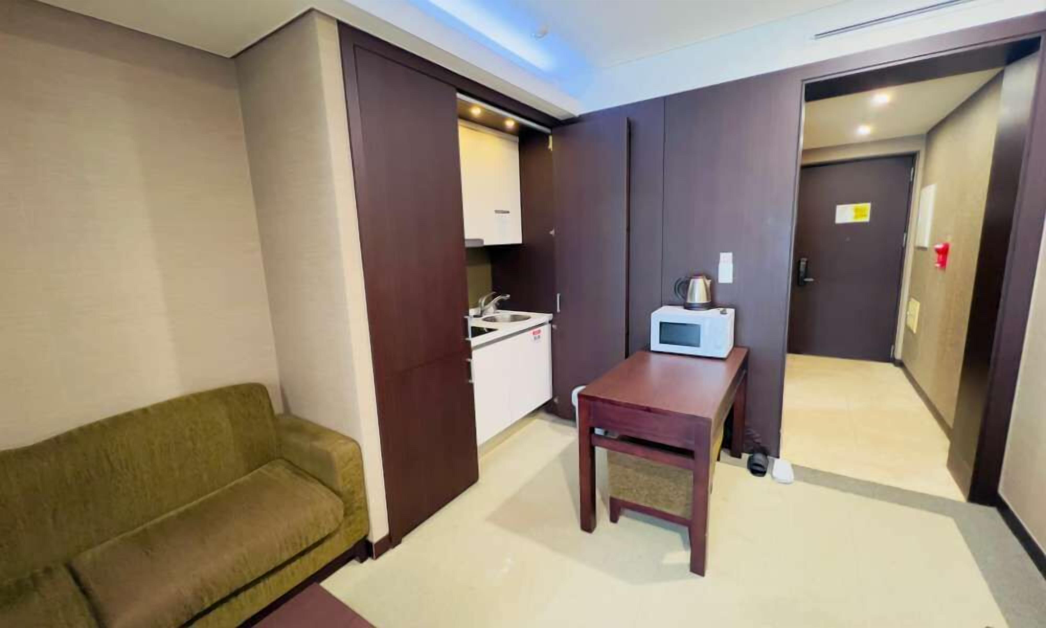 A compact hotel room with a kitchenette, a small table with a microwave, and a sofa.