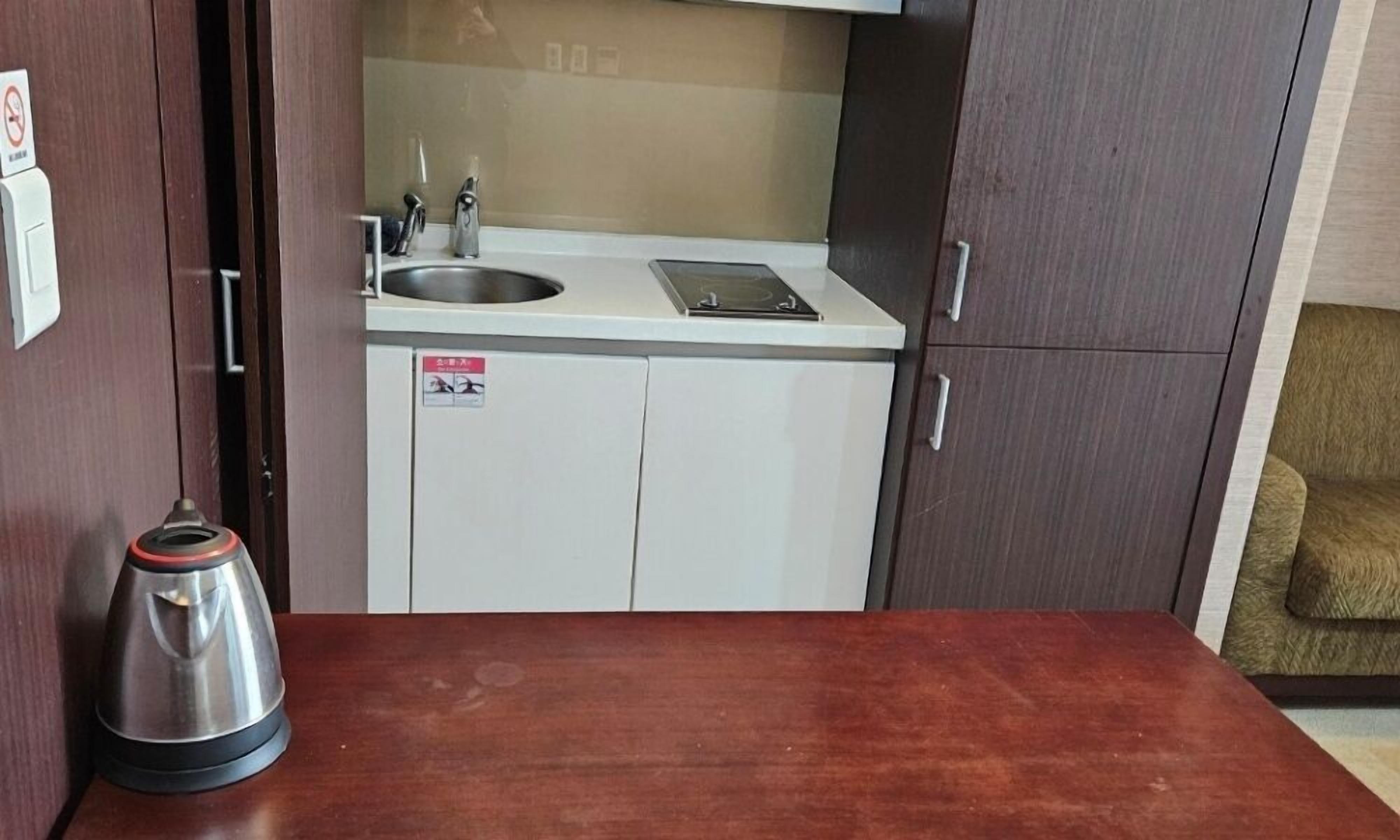 A compact kitchenette with a sink, a small stove, and a kettle on the counter.