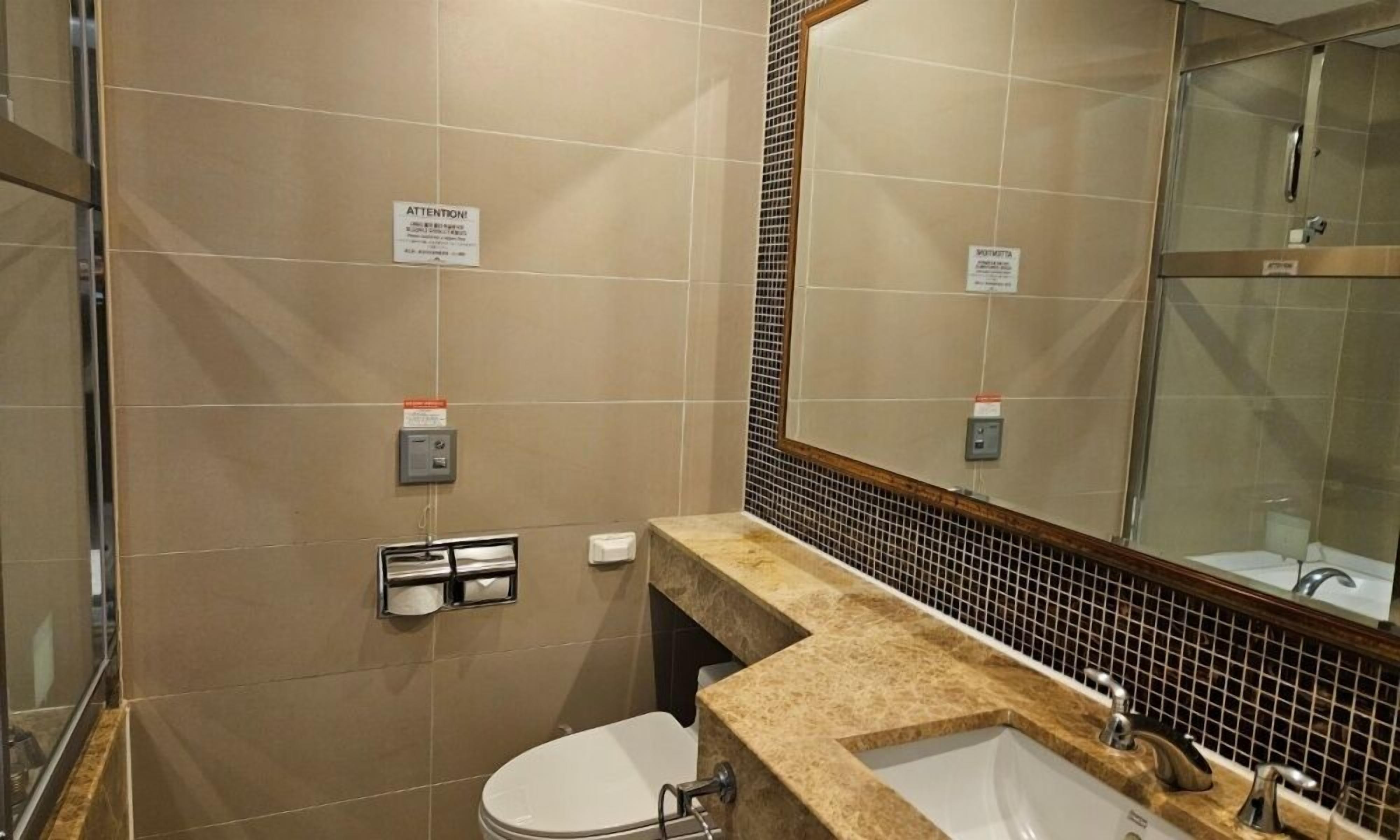 A bathroom with a toilet, sink, and mirror. There are signs on the wall and a towel dispenser.