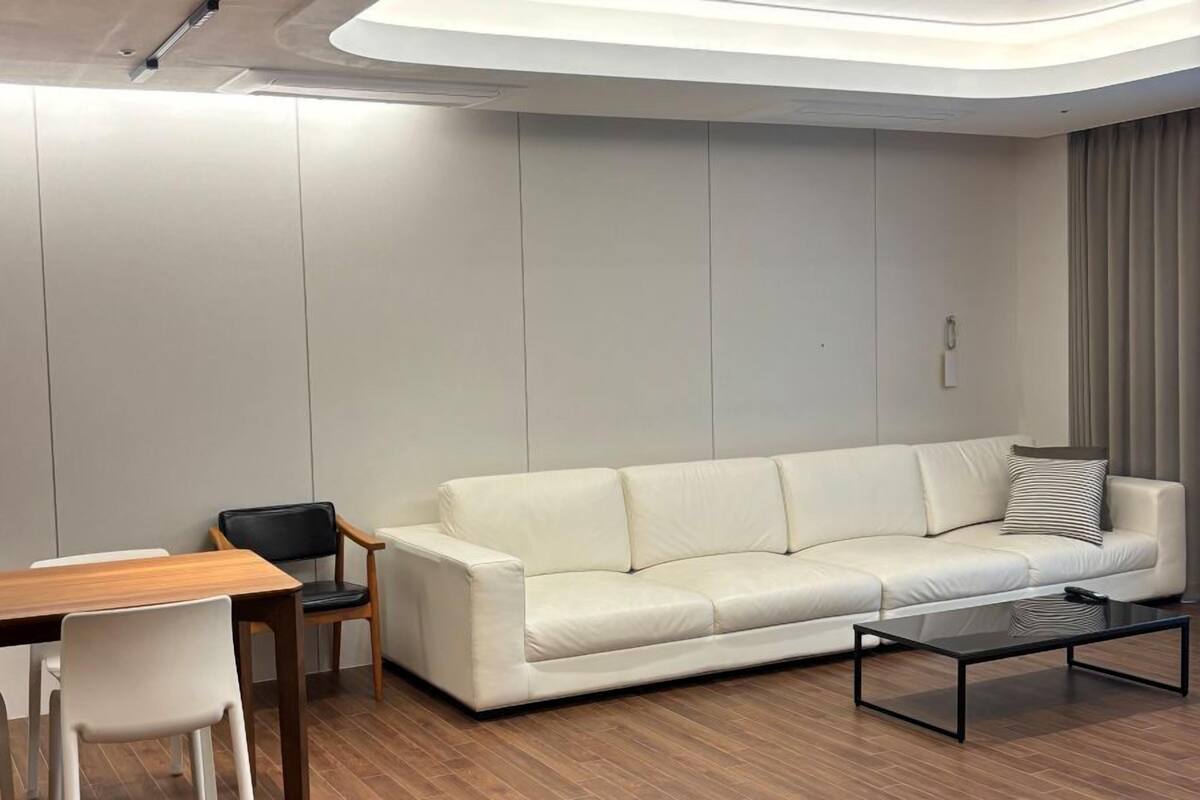 Una sala de estar moderna con un sofá de cuero blanco, una mesa de comedor de madera con sillas, y una mesa de centro de vidrio.
