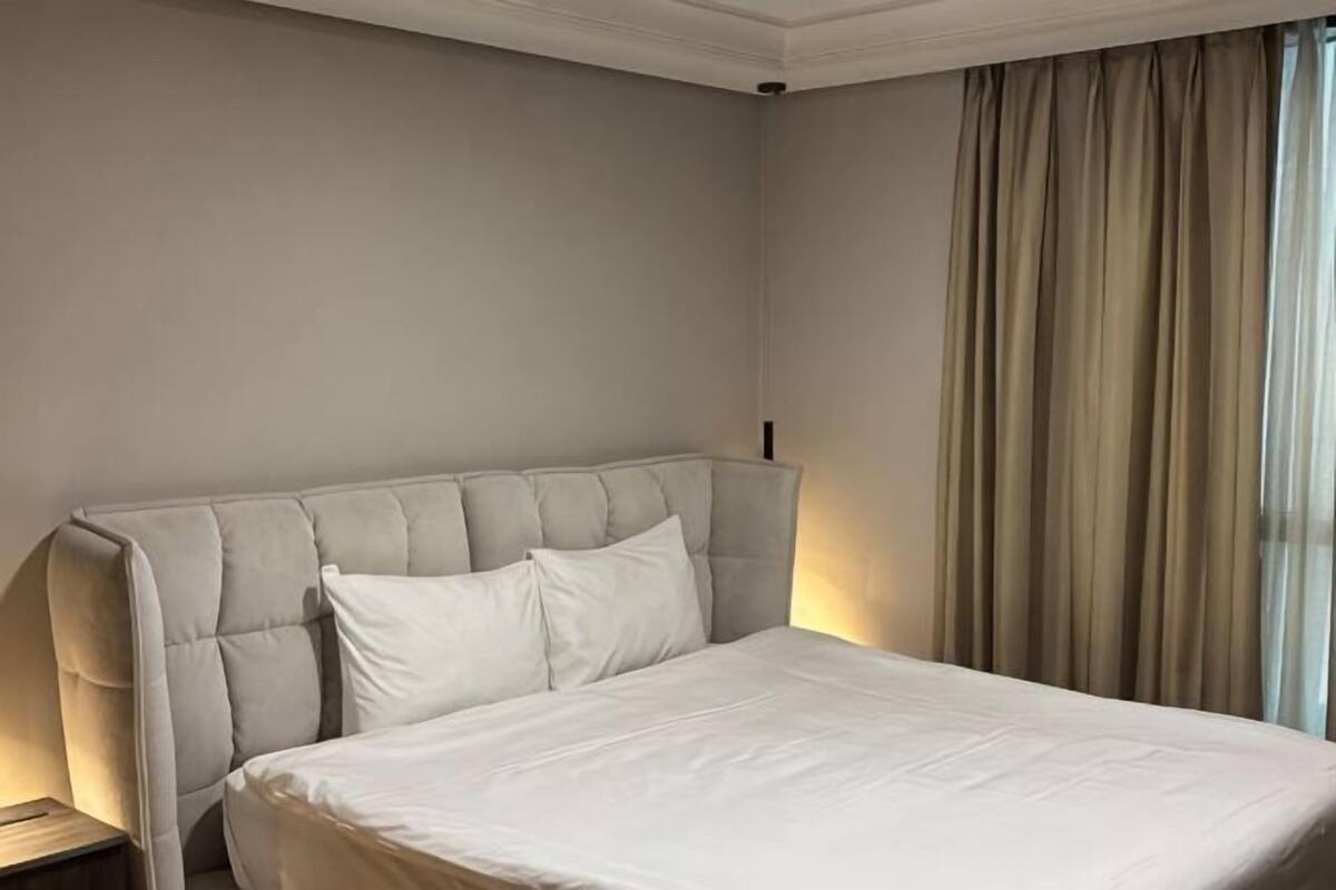 Una habitación de hotel con una cama grande, una mesita de noche y un ventanal con cortinas.