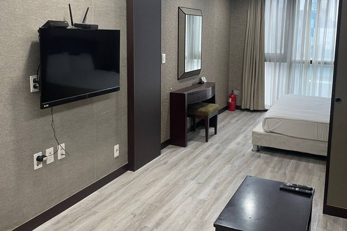 Habitación de hotel con televisión de pantalla plana en la pared, escritorio con silla, cama y una mesita pequeña.
