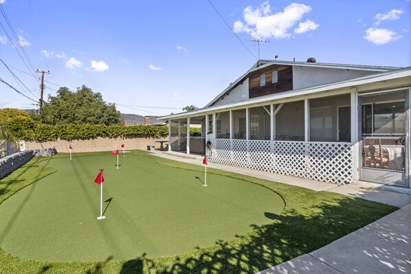 Une propriété résidentielle dotée d’un patio couvert, d’une pelouse avec un terrain d’entraînement au golf et d’une maison entourée d’une clôture blanche.