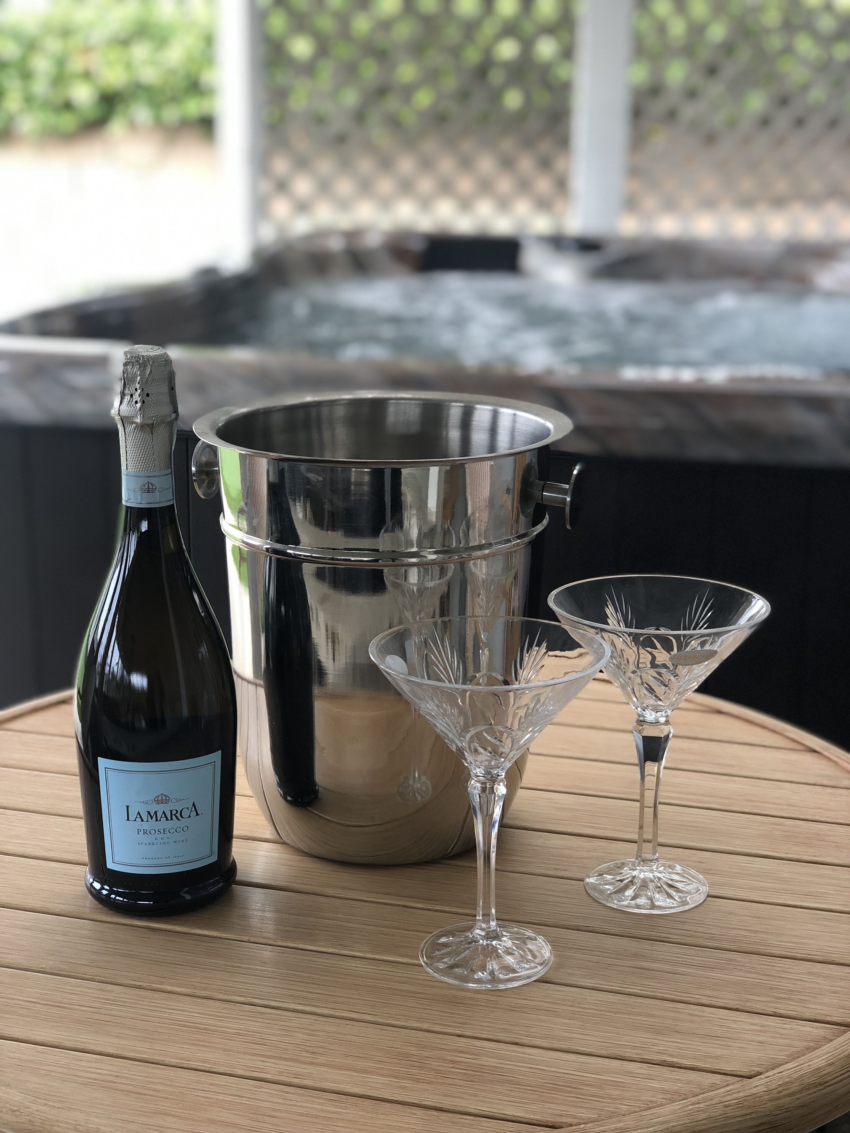 Lamarca Prosecco -pullo, hopeanvärinen jäähdytysastia ja kaksi martiniglassia puisella pöydällä.