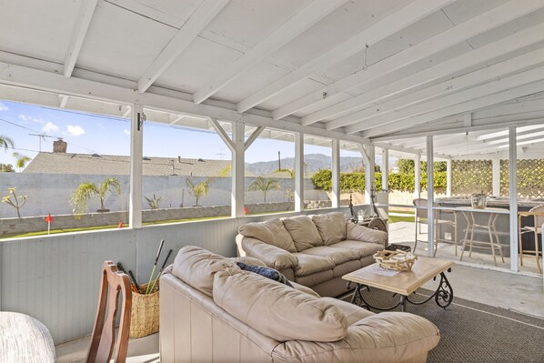 A covered patio area with beige sofas, a table, and a grill.