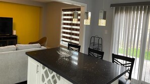 A modern kitchen with a black countertop, white cabinetry, and a dining area with a black chair and a basket. - Spacious 4 Bdrm House in Brampton (Brampton)