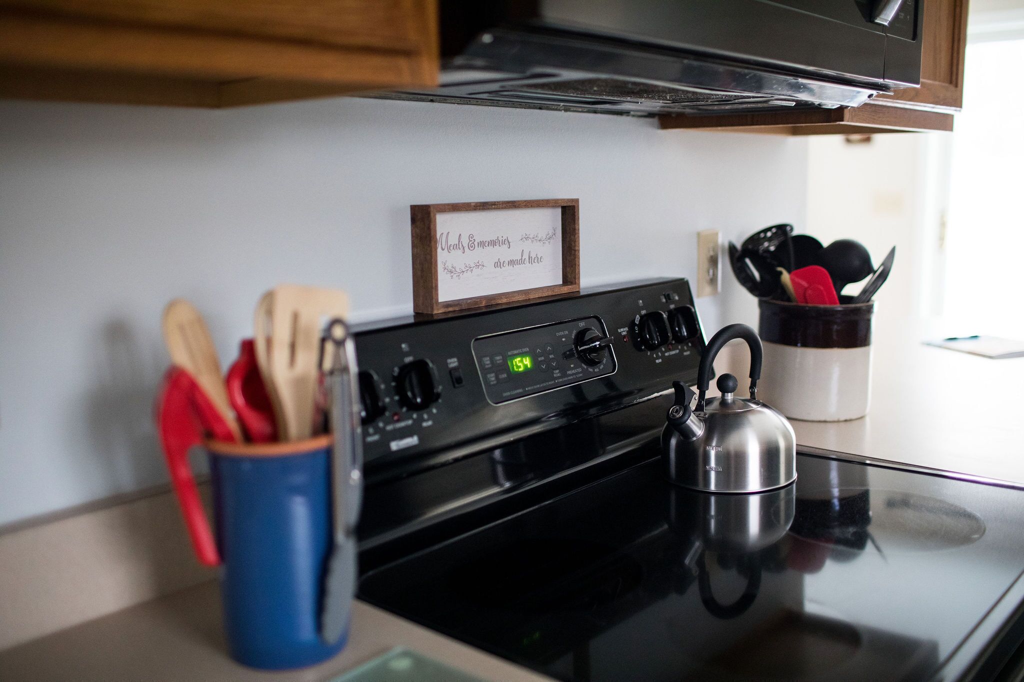 A kitchen with a stove, a kettle, and a sign that reads "Neal's Emblems are made here."