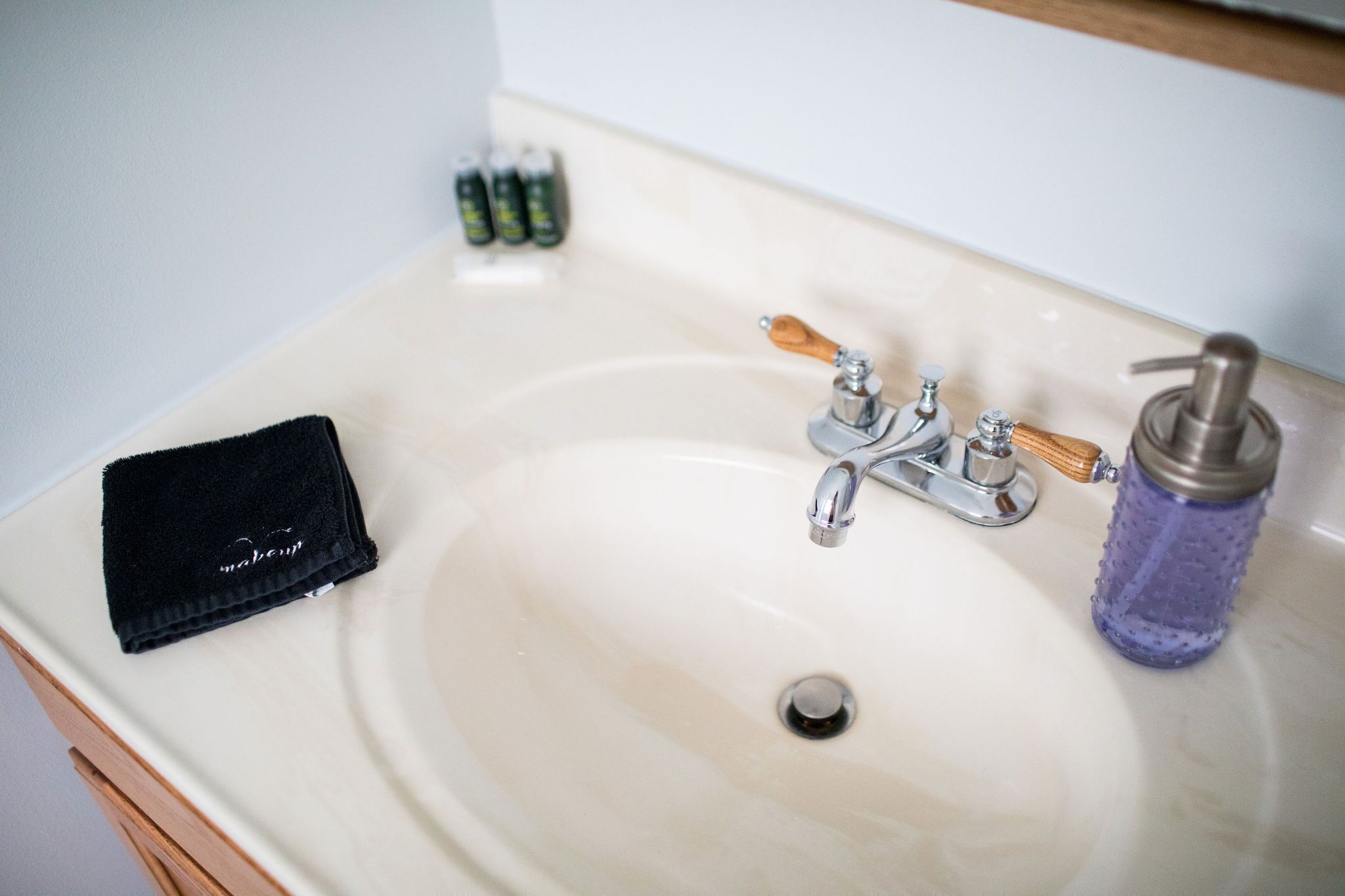 A bathroom sink with a black towel, a wooden-handled faucet, and a purple water bottle.