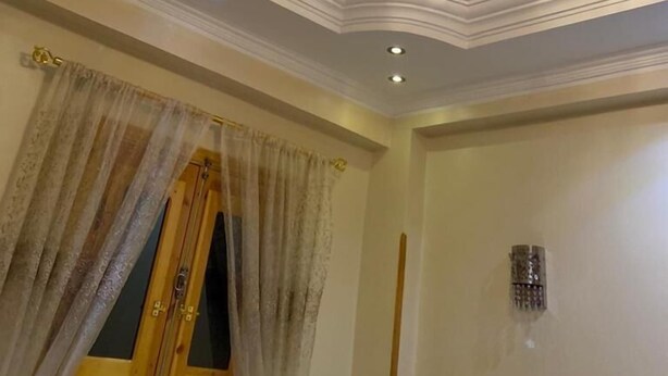 Una habitación con techo decorativo, una araña y una ventana con cortinas.