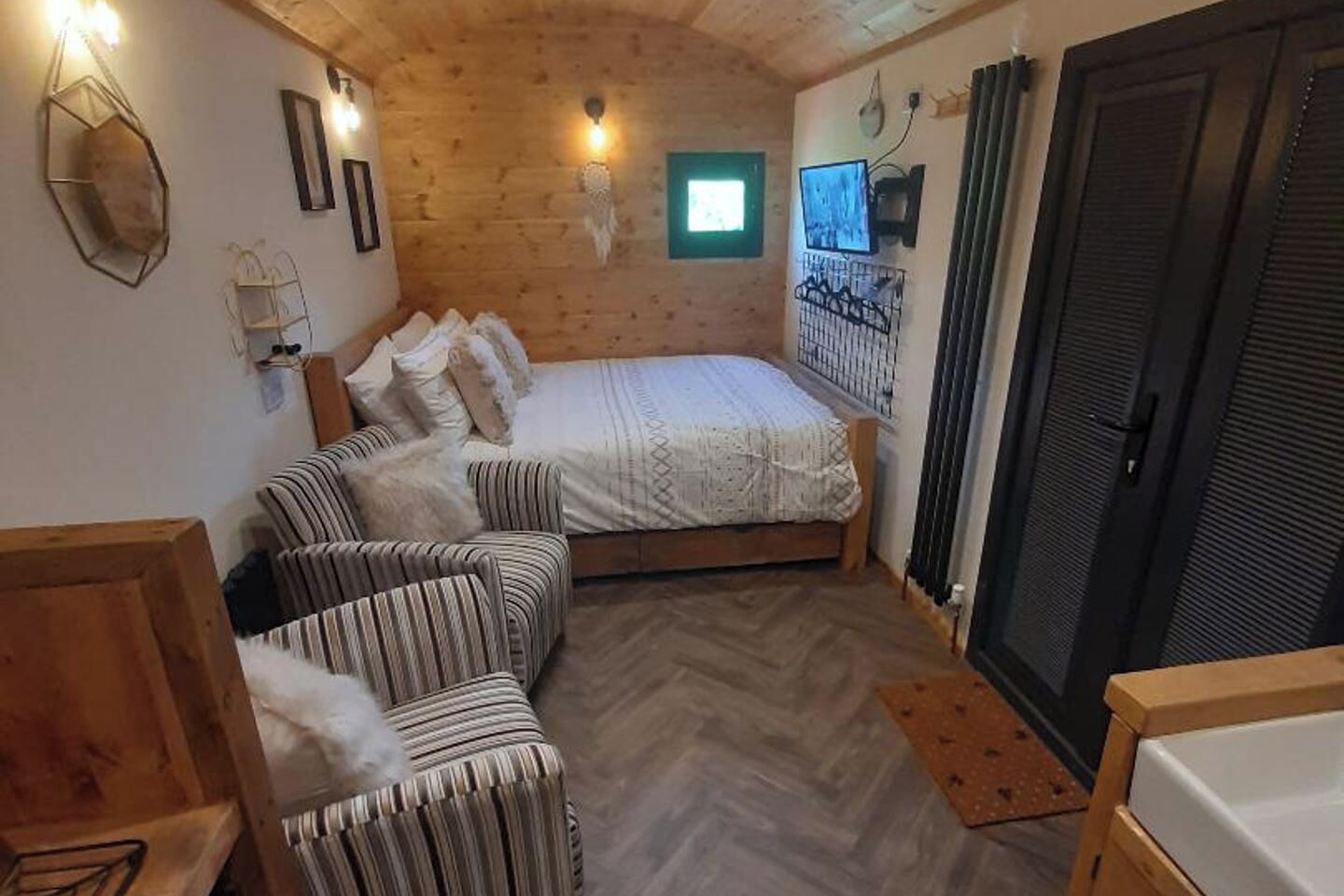 A cozy room with a bed, two striped sofas, a small window, and a TV on the wall.