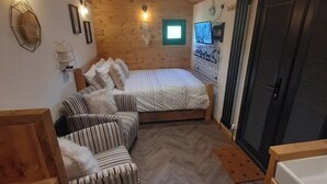 A cozy room with a bed, two striped sofas, a small window, and a TV on the wall. - Min yr Afon - Cabin - Sleeps 2 - Hot Tub - Parking (Anglesey)