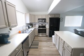 A modern kitchen with white cabinets, stainless steel appliances, and a wooden floor.