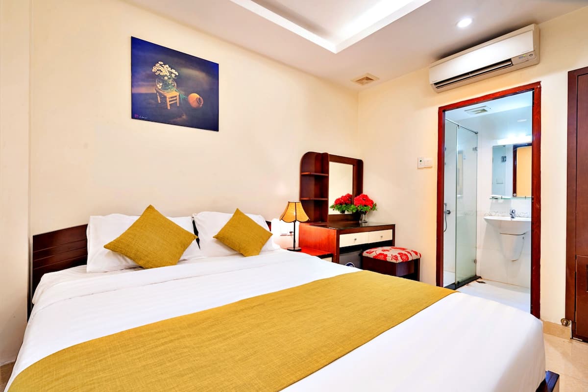 A hotel room with a bed, a nightstand, a mirror, a desk, and a bathroom visible through an open door.