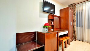 A hotel room with a wooden desk, a television mounted on the wall, a small wooden cabinet, a bench, and a pair of slippers in a shoe rack. - S79 Boutique Hotel by hostify (Ho Chi Minh City)