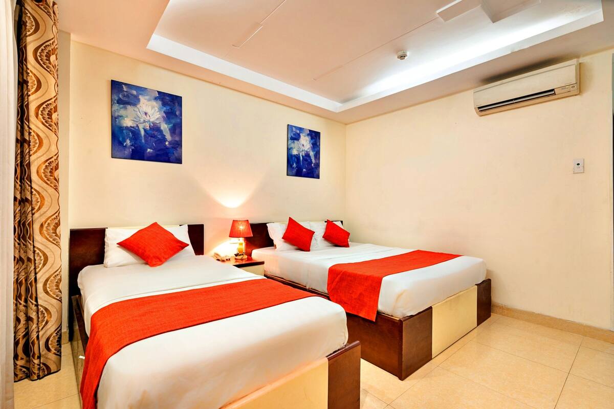 A hotel room with two beds, red bedding, a ceiling fan, and two wall-mounted air conditioning units.