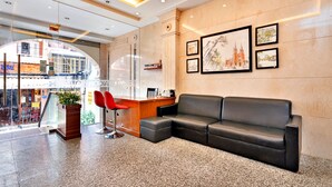 A lobby with a black leather sofa, red chairs, a reception desk, and framed artwork on the wall. - S79 Boutique Hotel by hostify (Ho Chi Minh City)